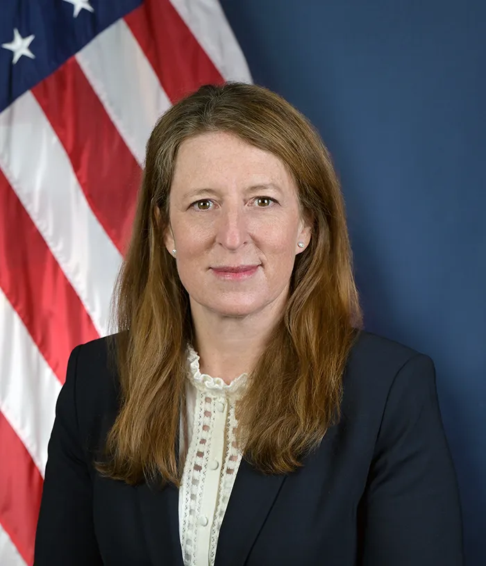 A portrait of Robin Hutcheson in front of an American flag.