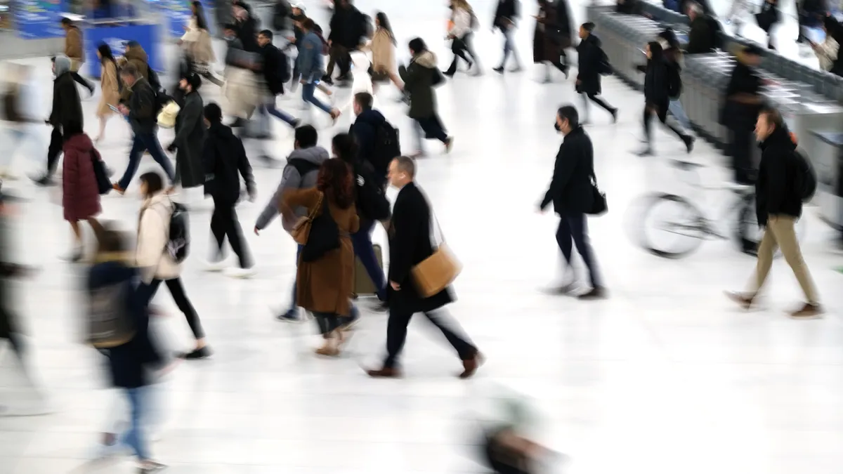 Many individuals are seen from above walking through a transit station.