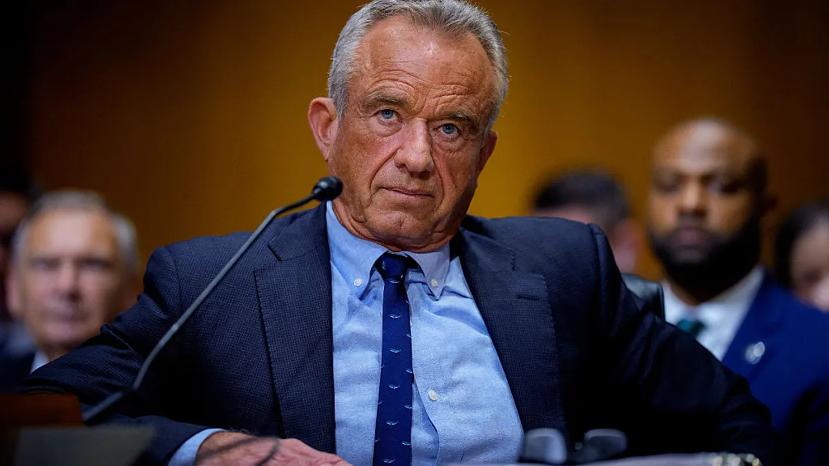 A person in a blue sit sits behind a desk at a hearing.