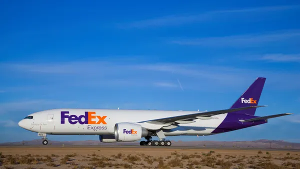 A FedEx branded airplane on a runway with a blue sky in the background.