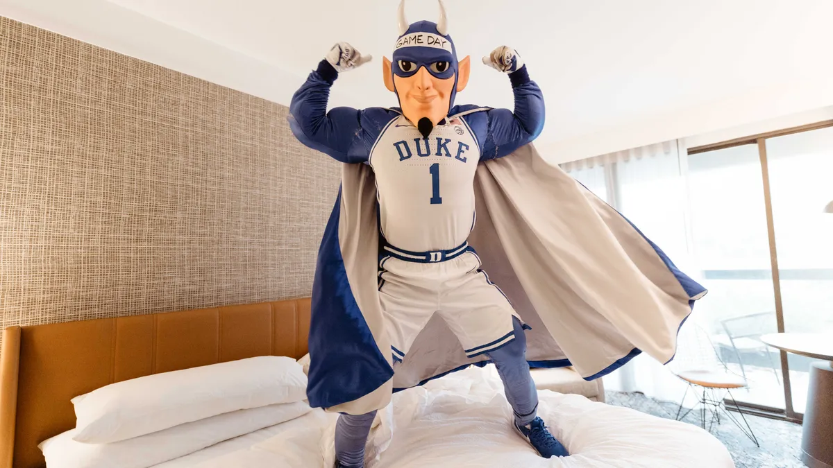 Duke Blue Devil mascot flexes on a Marriott hotel bed