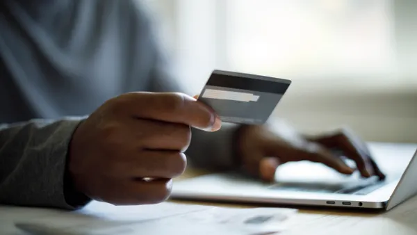 Close-up of person's hands, one hand holding a credit card and the other typing on a laptop.