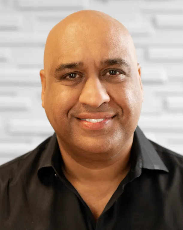 A person in a black shirt smiles in front of a white brick background