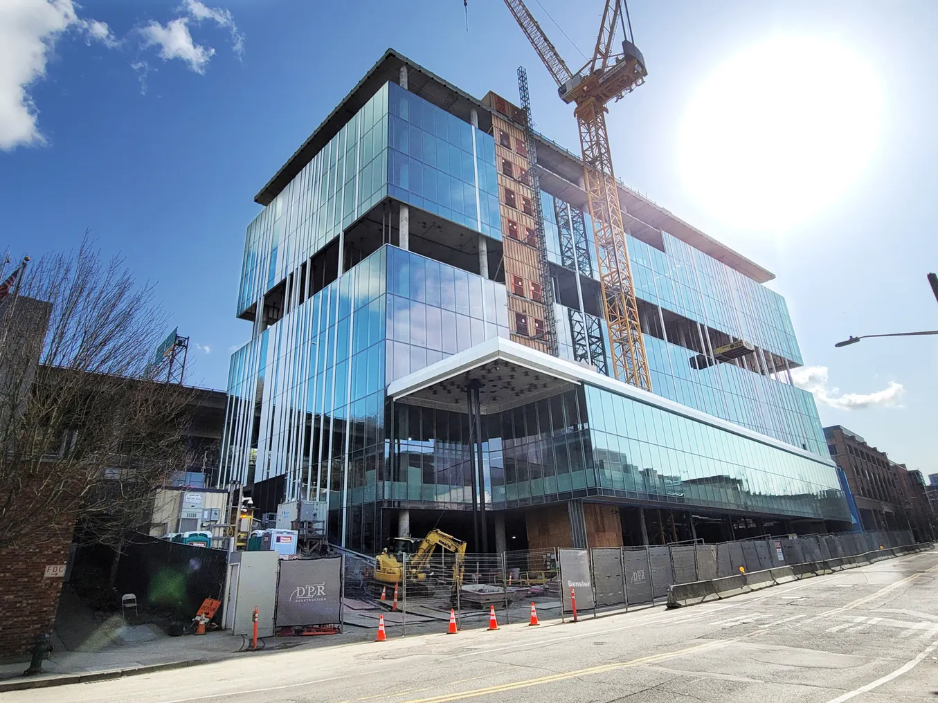 A yellow crane stands in front of a tall, shiny glass building that is mostly constructed.