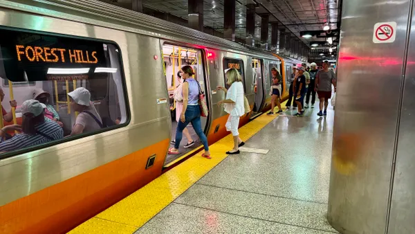 People in an underground subway station board a silver and orange train.