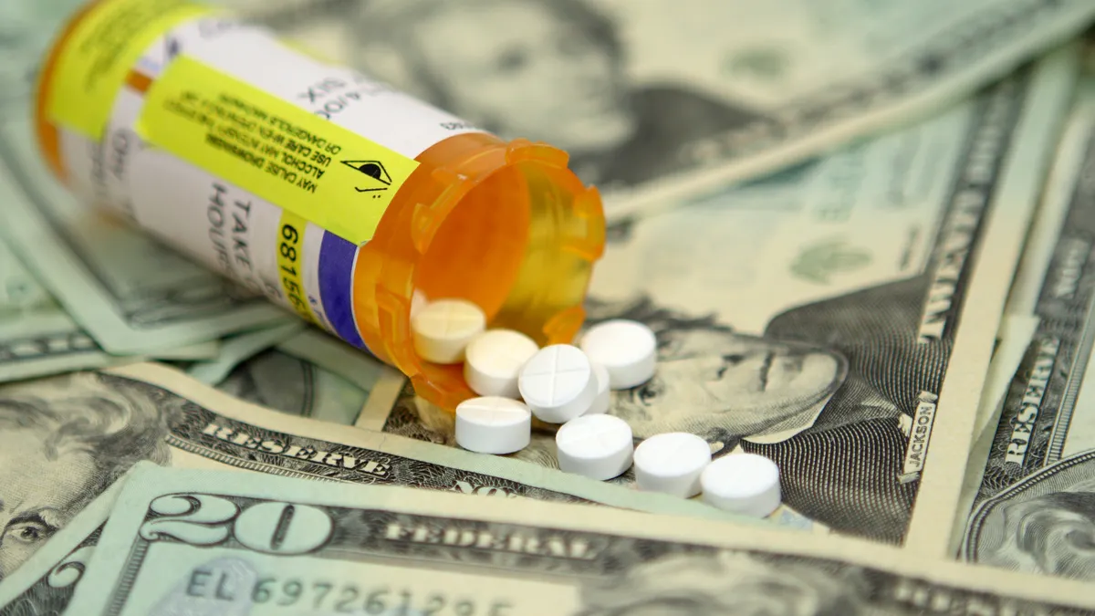 Prescription pills spilling out of the bottle on a background made of $20 bills.