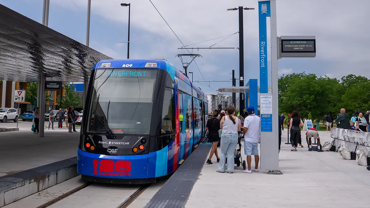 People on train station platform alongside a blue tram with a sign reading "Riverfront."