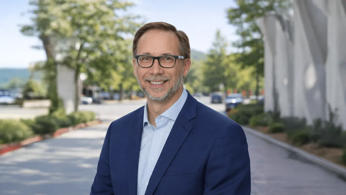 A head and shoulders photo of a person outside of a building, with a parking lot behind them.