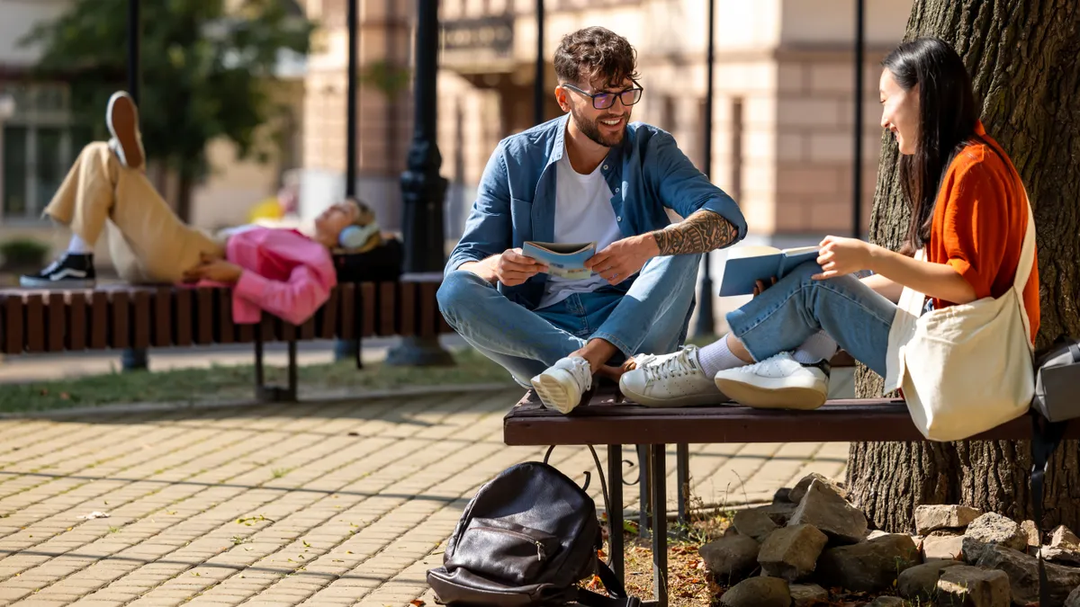 Two college students sit on a bench and talk.