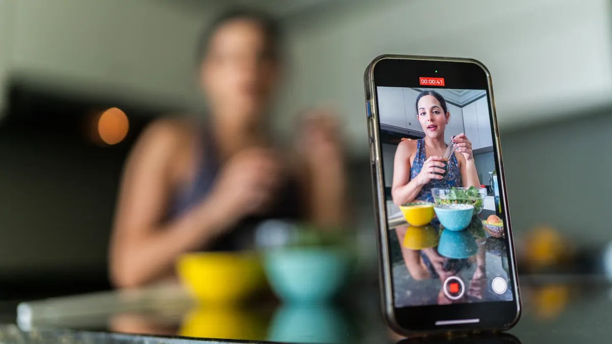 Close-up of a mobile phone recording a young woman vlog preparing salad in kitchen at home