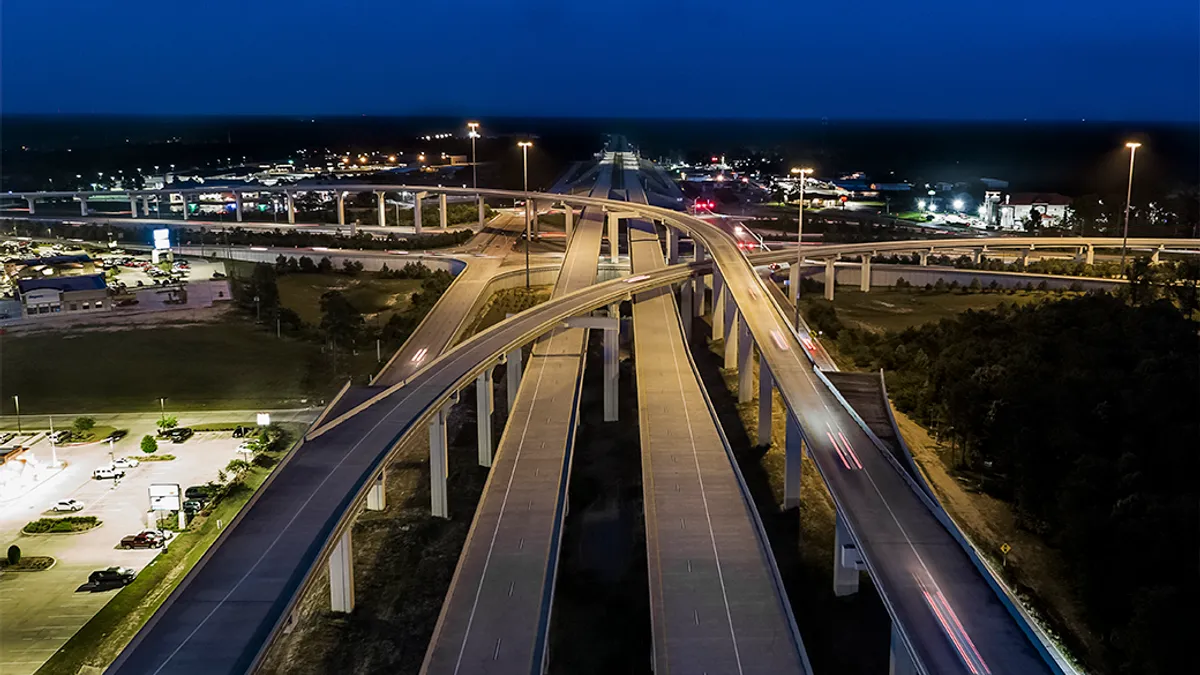 A birds eye view of a highway surrounded by a city with lights lit up and parking lots