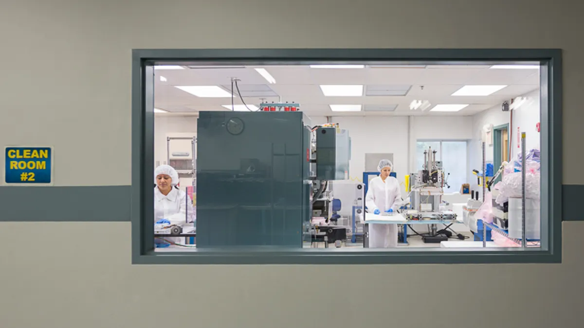 Two employees work in a clean room pictured through a window at UFP Technologies' Grand Rapids, Michigan, facility.