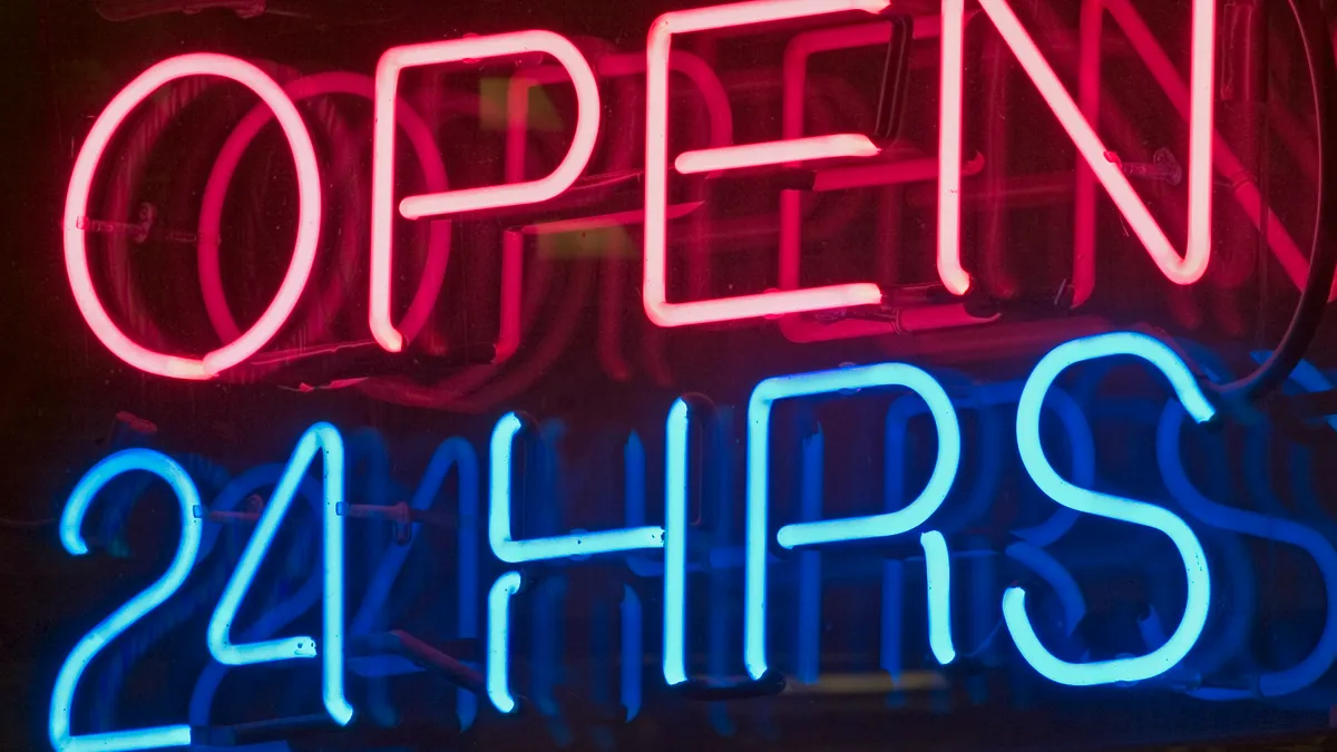 A photo of a neon sign in red and blue in a window that reads "open 24 hours."