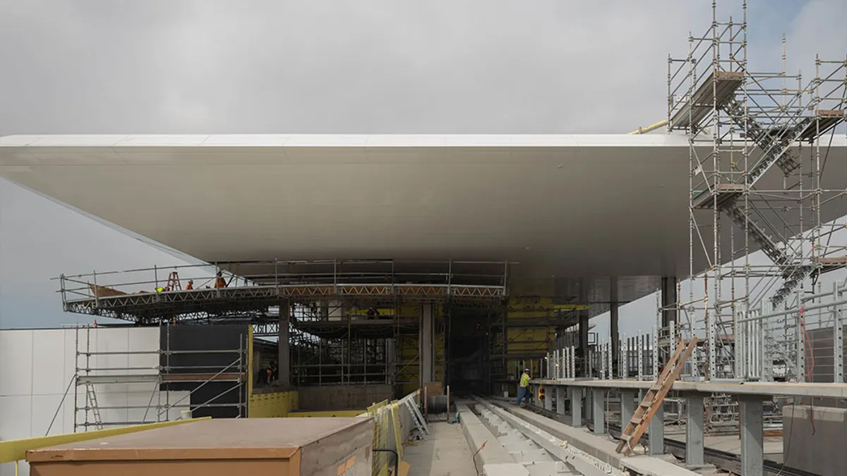 A thin white roof extends over scaffolding and train tracks.