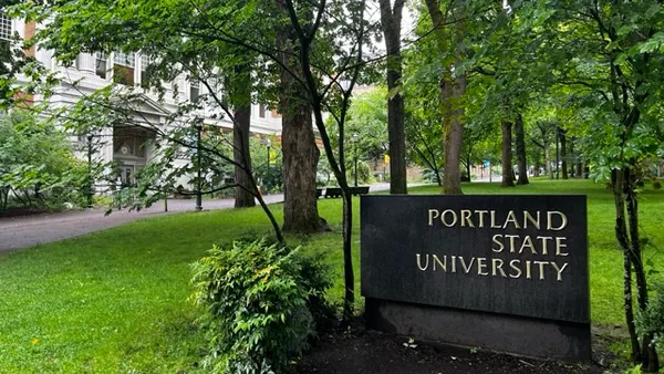 A large sign reading "Portland State University" with a grassy, rainy campus in the background