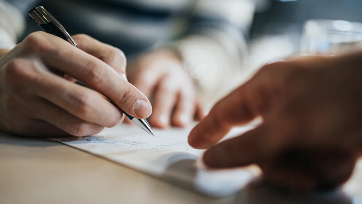 Close up of unrecognizable man signing a contract while someone is aiming at the place he need to sign.