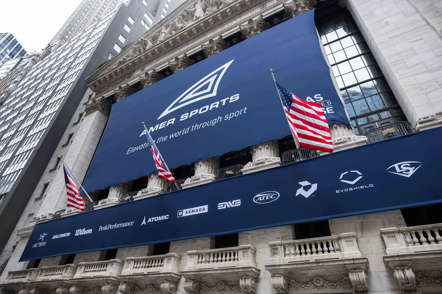 A blue Amer Sports banner hangs on a building, with American flags blowing.