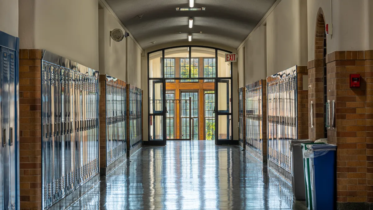 The hallway of a school leads to a stairwell and windows.