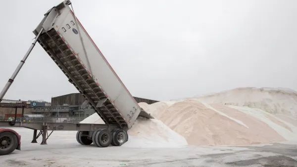 A truck dumps a load of road salt into a pile.