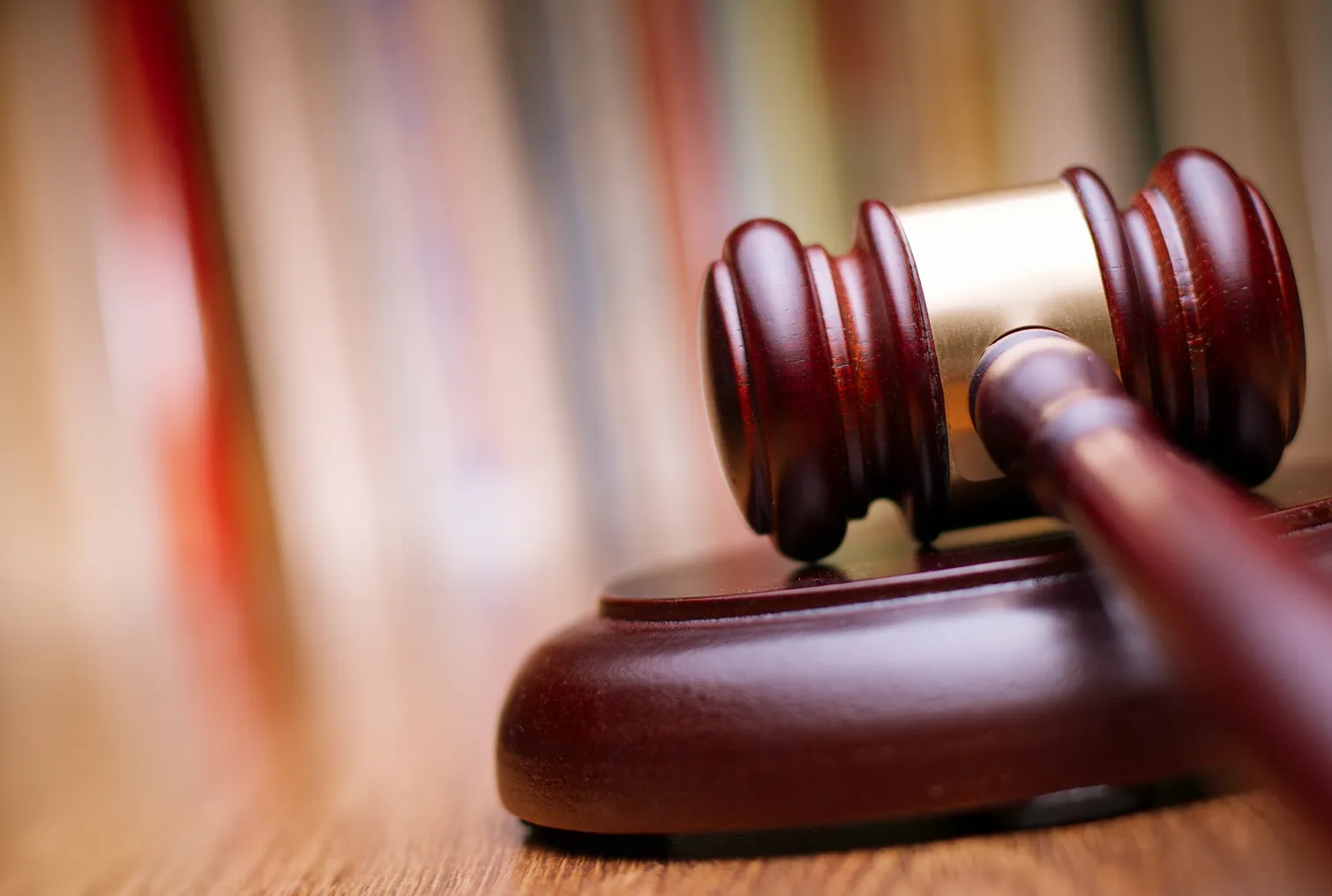 Close up shiny wooden law gavel in dark brown color on top of a wooden table in an office.