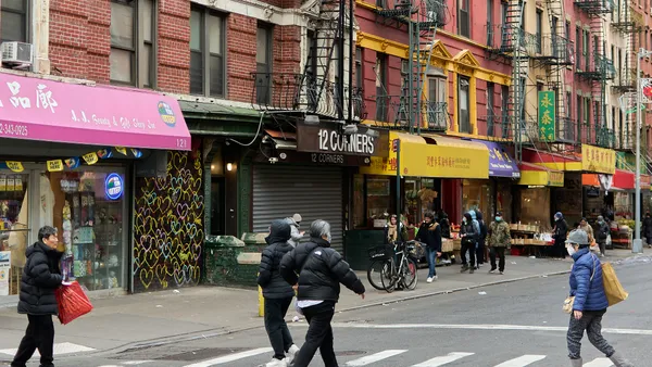 A city street lined with small storefronts. People walk across the street at a crosswalk.