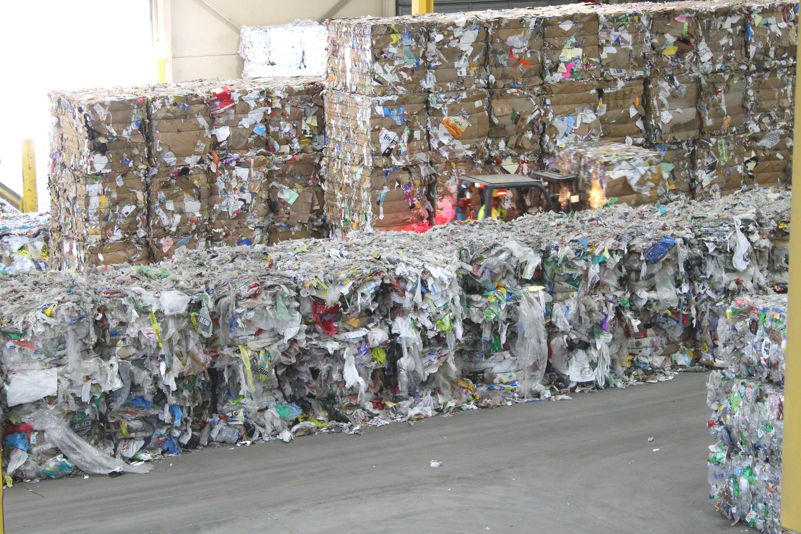 Bales of plastic film packaging are piled next to bales of other plastics and cardboard.