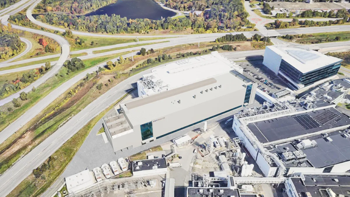 A skyshot and rendering of a large, white building amid other industrial sites and open grass and roads.