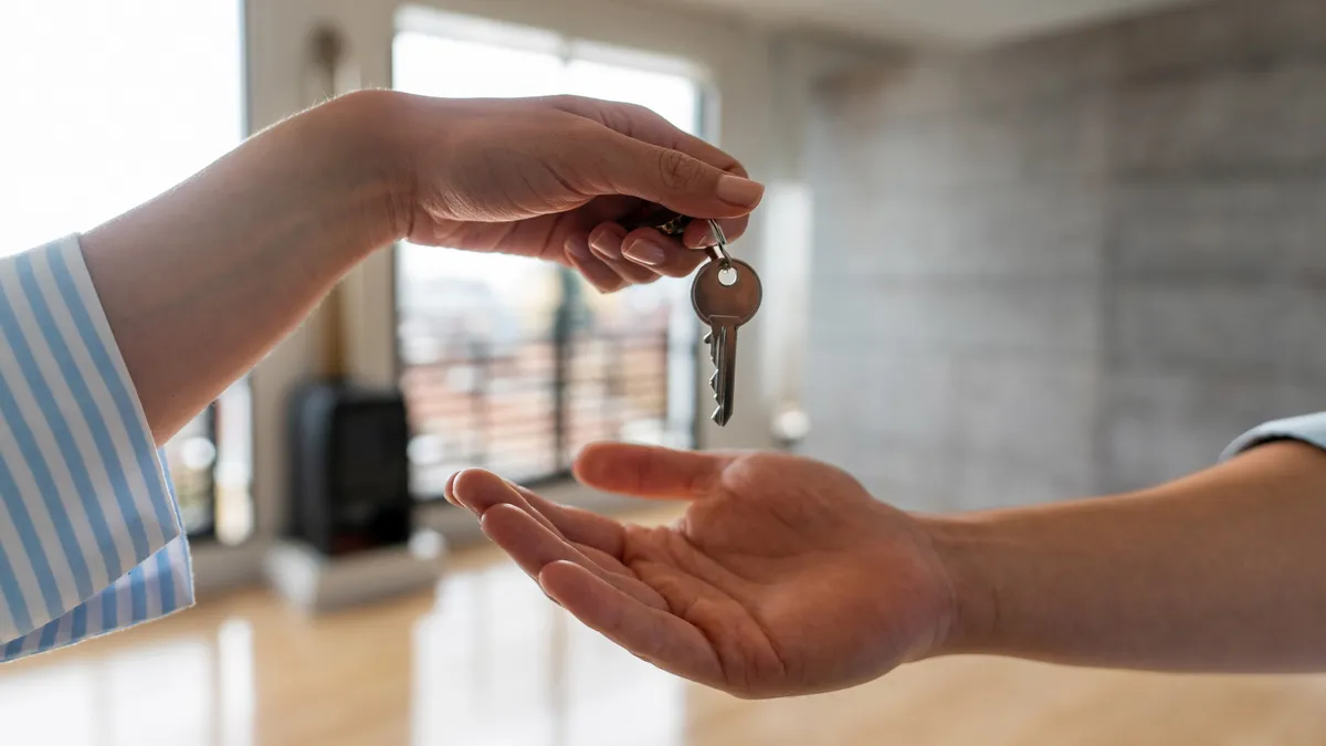 Two hands are shown against a home background, one person is handing a key to another.