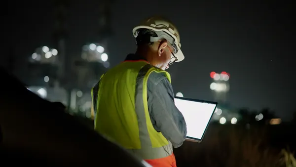 A construction worker at night looks at their laptop.