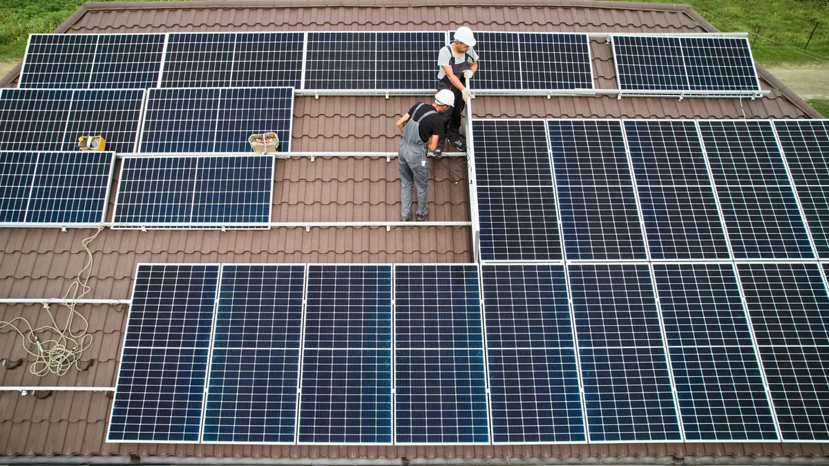 Engineers in helmets install a solar panel system on a roof.