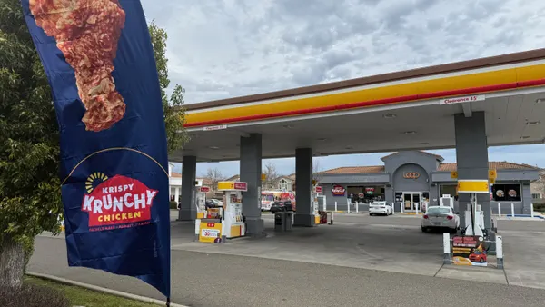 A photo of a flag out in front of a convenience store. The flag says "Krispy Krunchy chicken." A sign over the door of the convenience store says Loop.