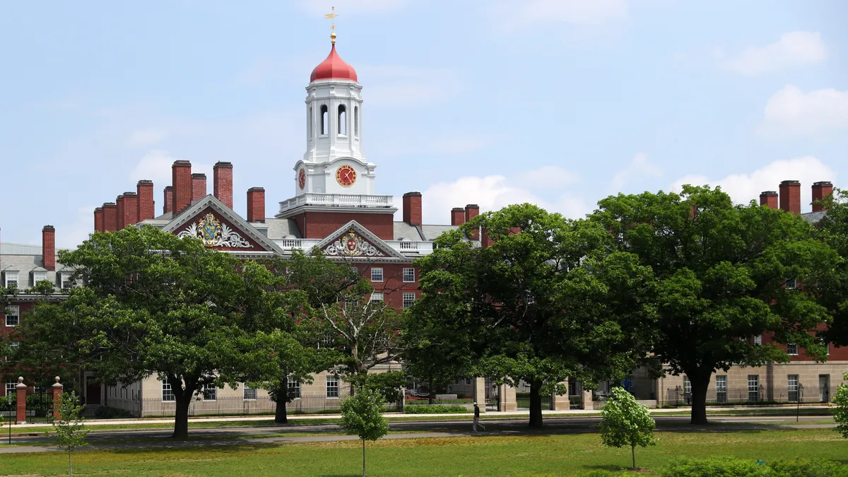 A brick building with many smokestacks sits behind green leafy trees.