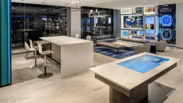 The stone and glass interior of a modern bank branch is shown, with seating and tables filling the room.