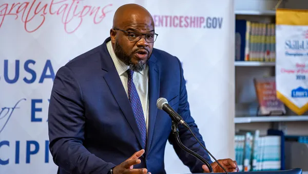 A man in glasses speaks at a podium to an audience out of frame.