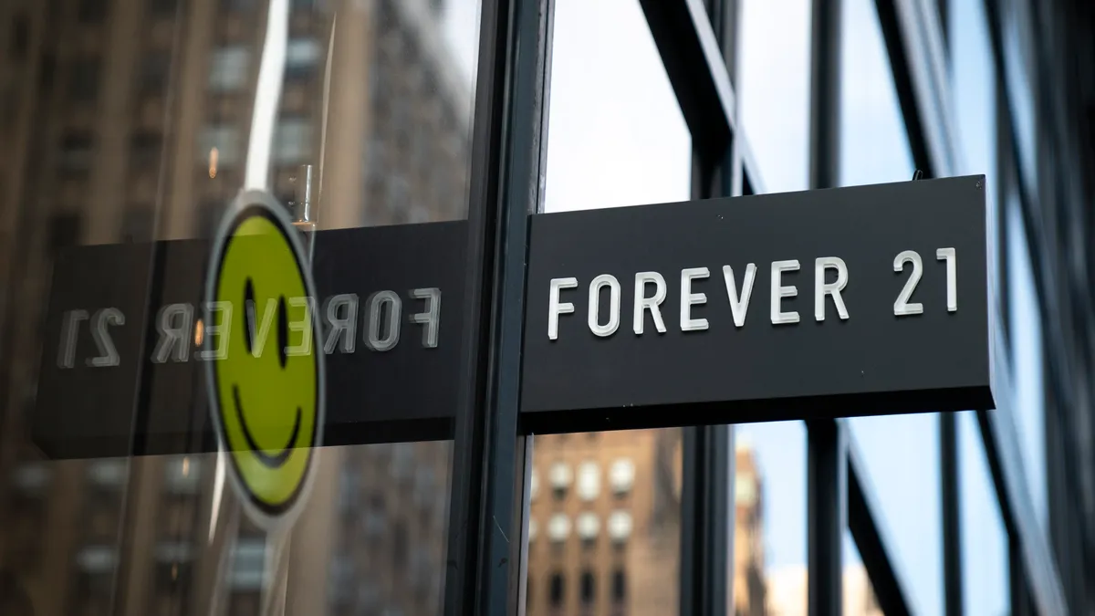 A sign for Forever 21 is pictured and a smiley face is reflected through the store's window.