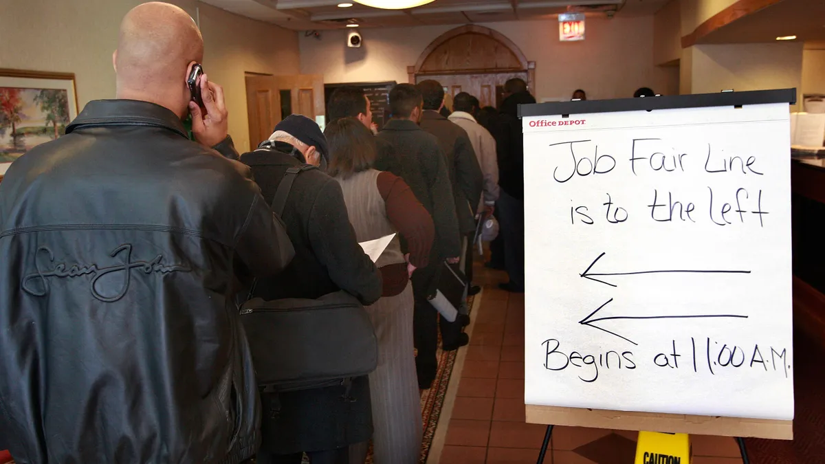 People stand in line with a sign directing them where to stand for seeking jobs