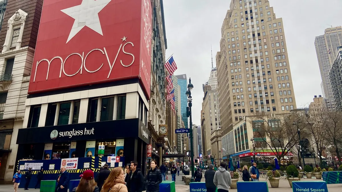 A busy city corner with people, buildings, trees and streetposts.