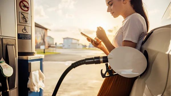 Woman leaning against car while pumping gas.