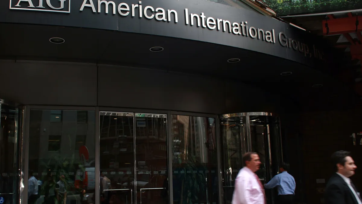 People walk in front of a building with glass doors and a sign across the top that reads: "American International Group."