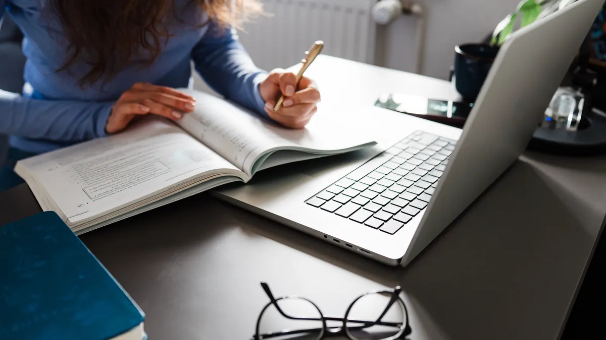 Woman Studying With Laptop And Open Book At Desk