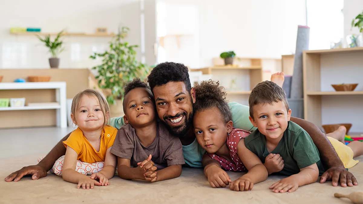 Group of small nursery school children with man teacher on floor indoors in classroom, looking at camera