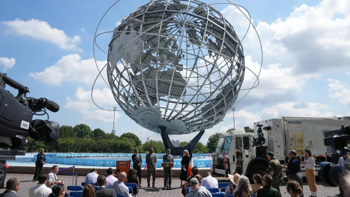 Large metal globe sculpture behind a group of people standing at a press conference