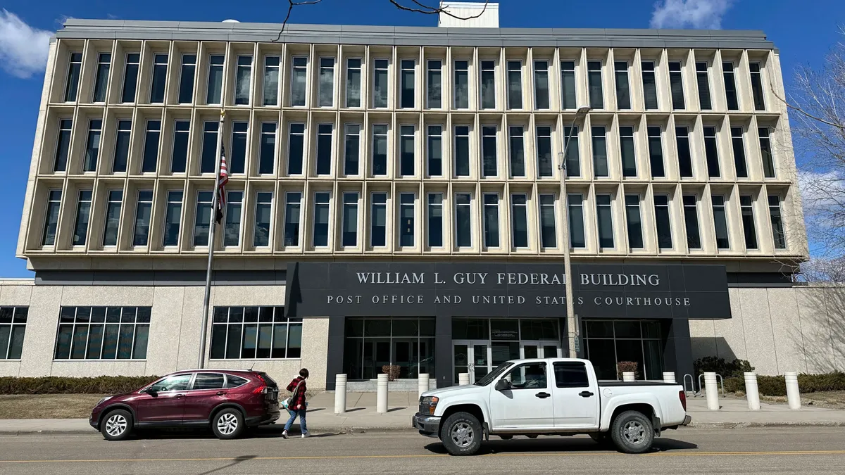 The front view of a gray municipal building, a sign reads, "William L. Guy Federal Building Post Office and United States Courthouse".