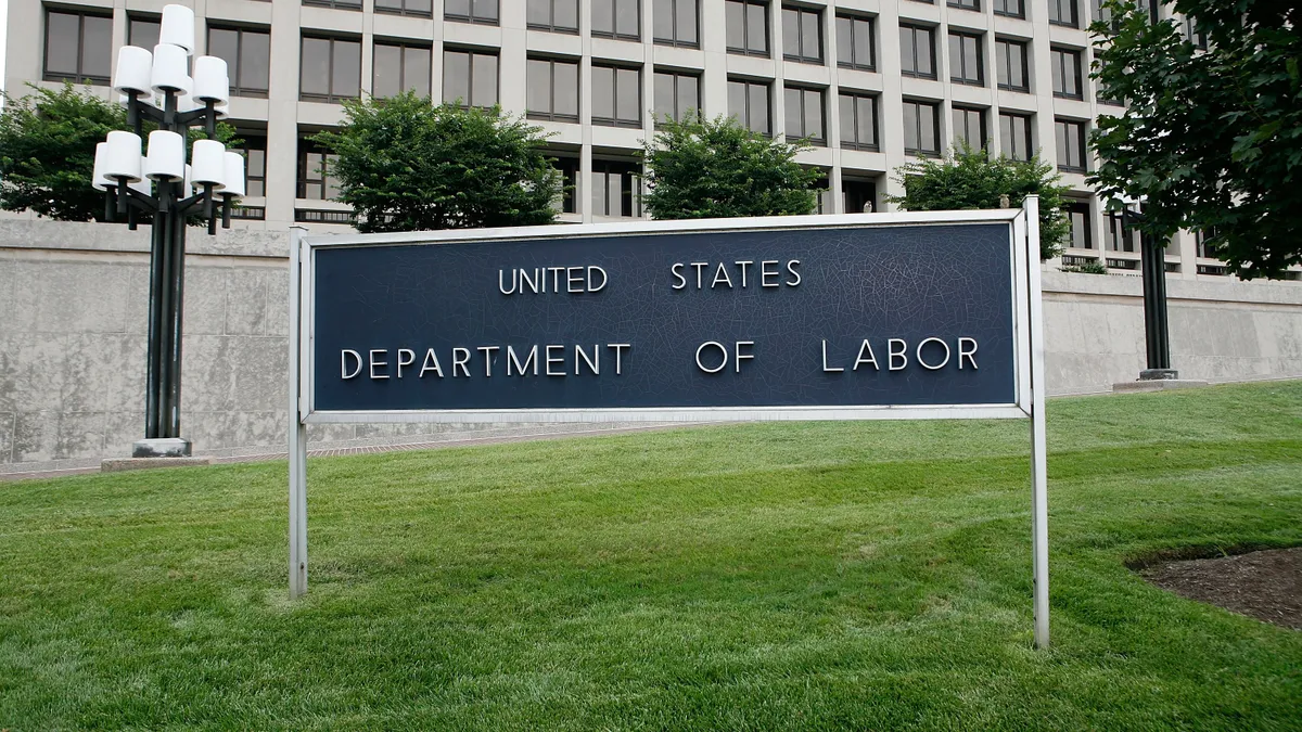 A dark Department of Labor sign in front of a white building with windows.