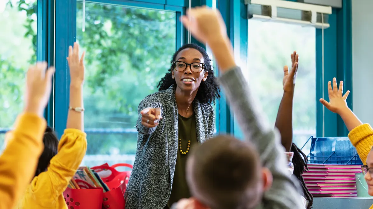 Teacher in classroom points to student raising hand