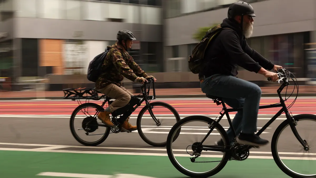 Two electric bikes with riders on a street pavement.