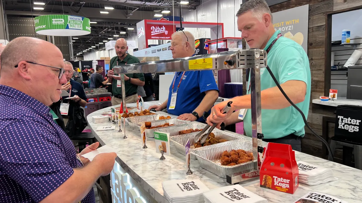 A worker offers a sample of Tater Kegs potato snacks to a show attendee