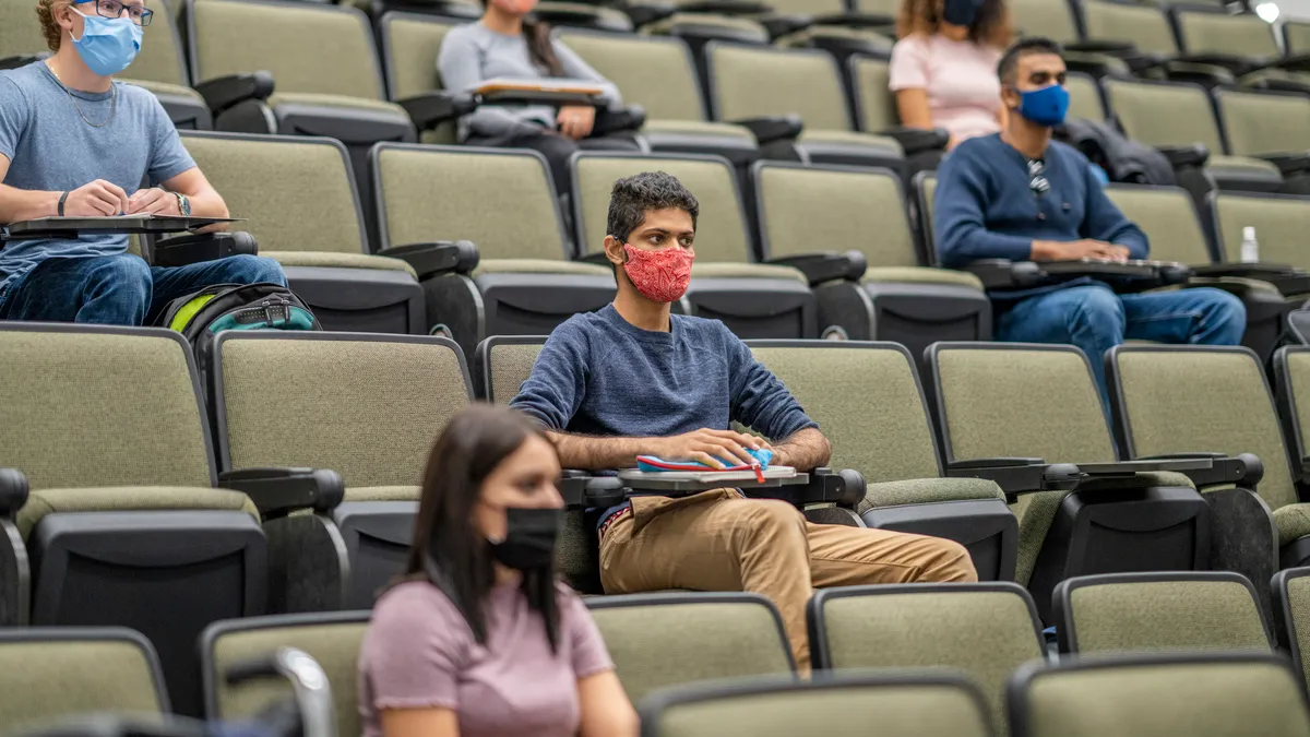 College students sitting in a lecture hall keeping social distance during the COVID-19 pandemic and wearing masks to protect from the transfer of germs.