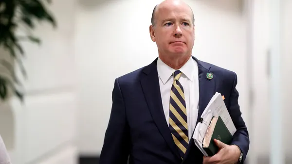 Robert Anderholt walks down a hallway holding a book and papers to his chest.