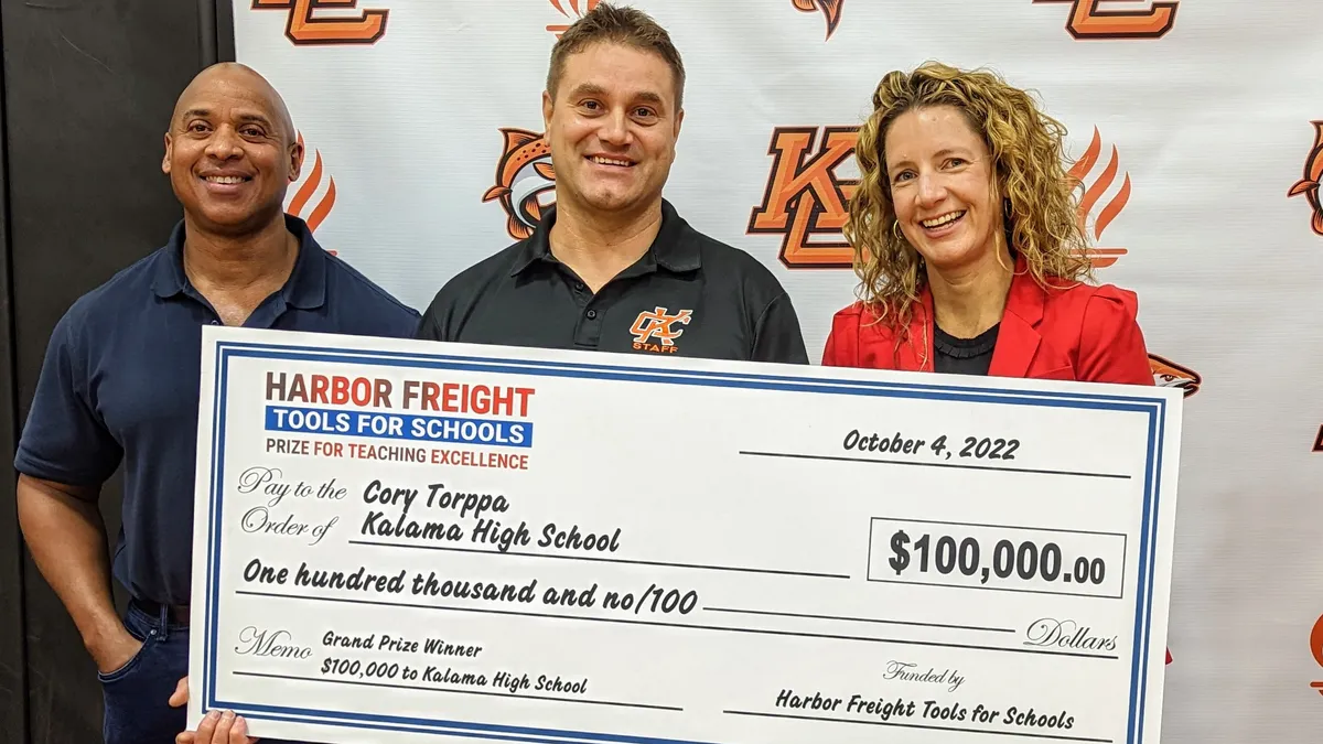 Three people pose for a photo while holding a large, prize money check.